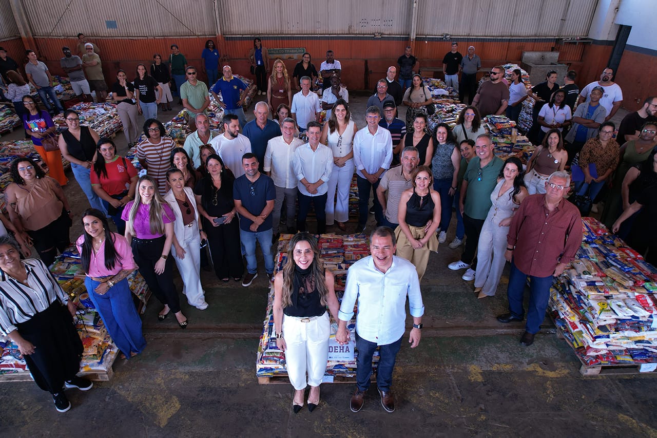 Foto mostra pessoas em frente aos alimentos arrecadados. 